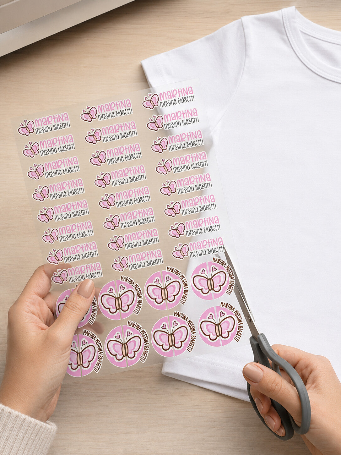Foglio di etichette termoadesive MIA con farfalla rosa e nome Martina, accanto a una t-shirt bianca